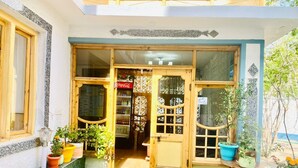 A building entrance with a Coca-Cola refrigerator, potted plants, and a green mat. - SIT Ladakh Horizon  (Leh)