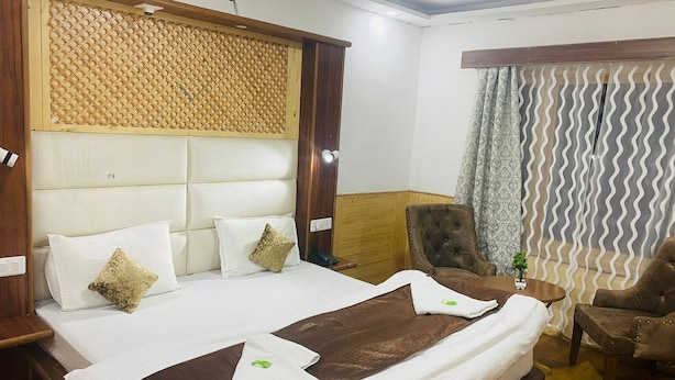 A hotel room with a large bed, a wooden headboard, a brown armchair, a small table with a plant, and a curtain with a wavy pattern. - SIT Ladakh Horizon  (Leh)