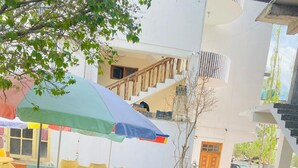 A patio area with artificial grass, wicker chairs, and a large umbrella providing shade. - SIT Ladakh Horizon  (Leh)
