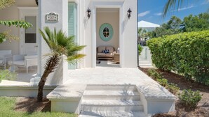 A white building with a porch, a palm tree, and a view of a house with a white roof.