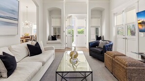A spacious living room with a glass coffee table, a sofa, a dark armchair, and a wicker ottoman.