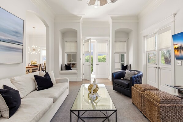 A spacious living room with a glass coffee table, a sofa, a dark armchair, and a wicker ottoman.