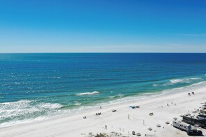 A beach with white sand, clear blue water, and a few people and vehicles.