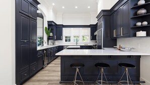 A modern kitchen with dark cabinetry, a large island with stools, and a view to the outside.