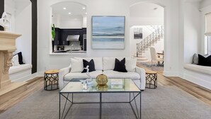A modern living room with a white sofa, a glass coffee table, and a painting on the wall.