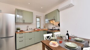 Una cocina moderna con armarios verde claro, un refrigerador de acero inoxidable y una zona de comedor preparada para una comida.