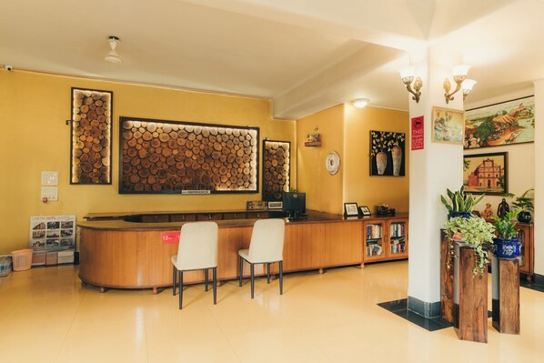 Un mostrador de recepción con dos sillas, un panel de madera en la pared y una estantería con libros y objetos decorativos.