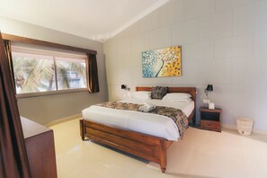 A bedroom with a wooden bed, a nightstand, a wall-mounted painting, and a window with curtains. - Casa De Cris (Cavelossim)