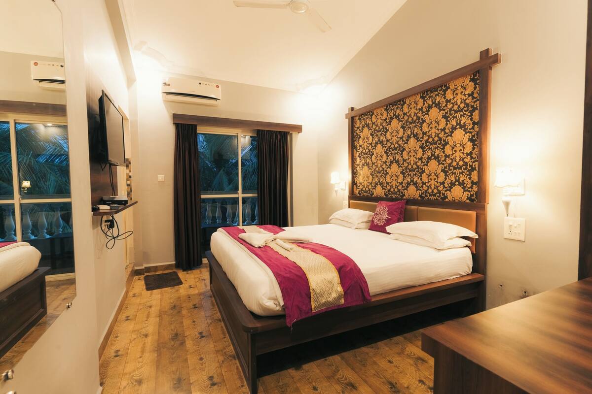 Quarto de hotel com cama, televisão, ar condicionado, janela com cortinas e um painel decorativo na parede.