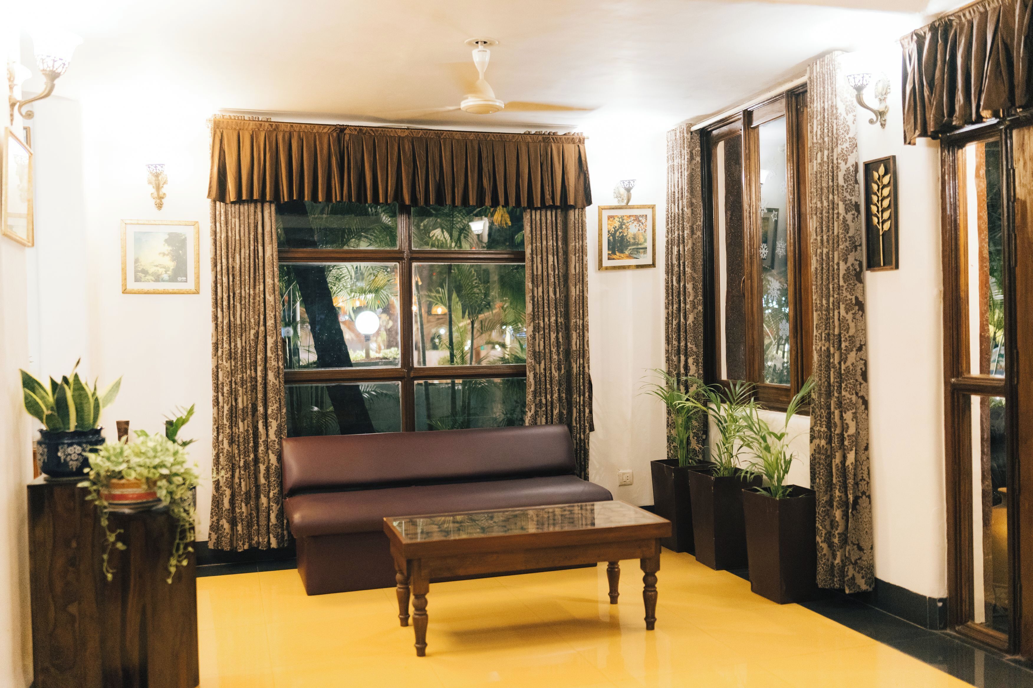 Una habitación con un sofá marrón, una mesa de centro de madera y un ventanal con cortinas.