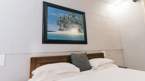 A bedroom with a bed, white linens, a wooden headboard, a framed picture of a beach scene, and a nightstand with a lamp. - Casa De Cris (Cavelossim)