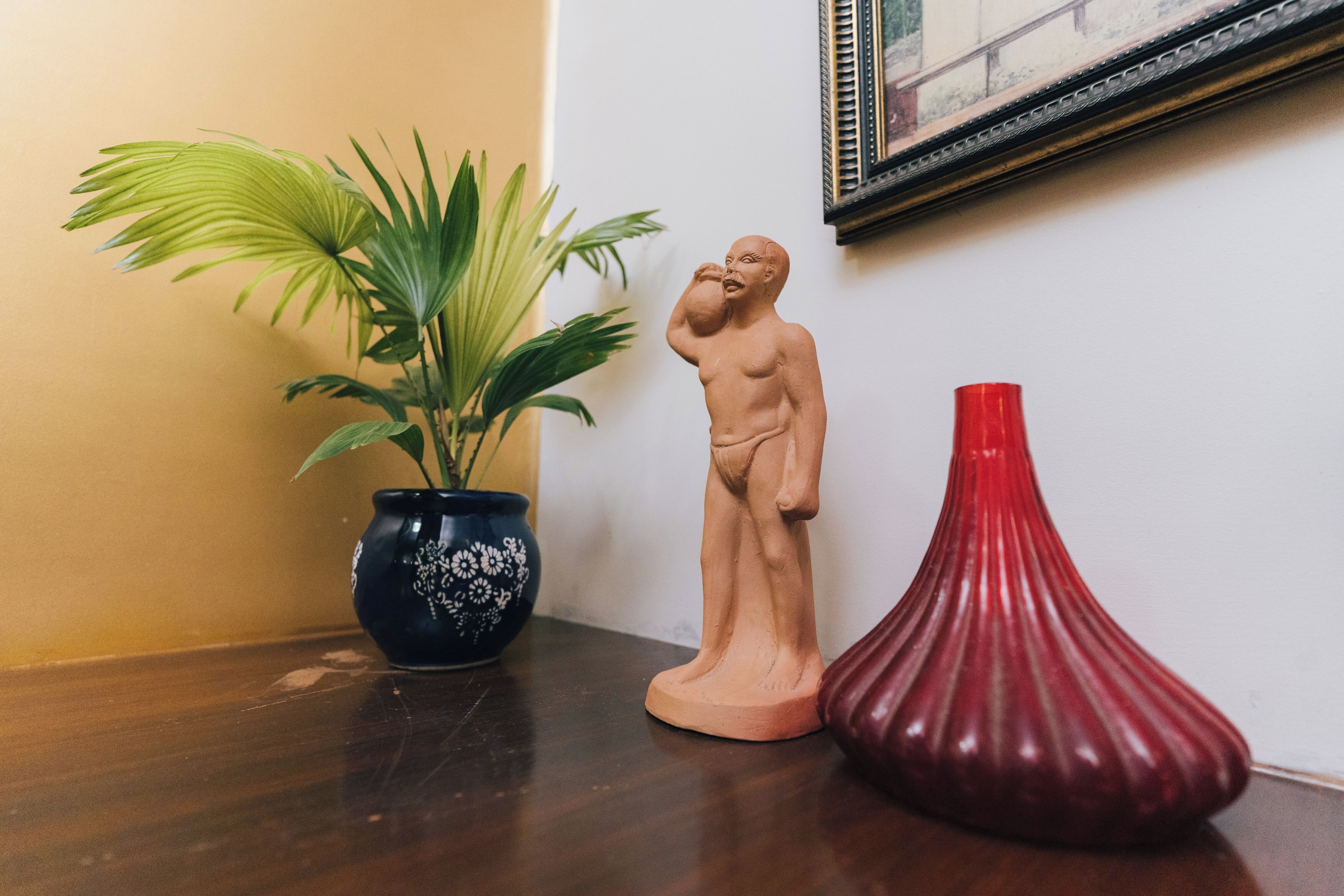 A wooden statue, a potted plant, and a red vase on a wooden surface.