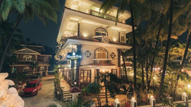 A multi-story hotel with a balcony, palm trees, and a red car parked in front. - Casa De Cris (Cavelossim)