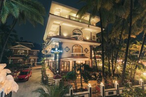 A multi-story hotel with a balcony, palm trees, and a red car parked in front. - Casa De Cris (Cavelossim)