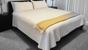 A bedroom with a bed, two bedside tables, a lamp, a window with blinds, and a wall-mounted artwork.