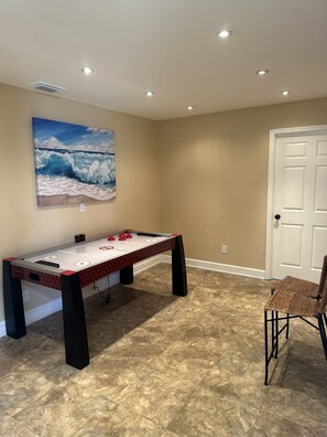 A room with a foosball table, a wall-mounted painting of a wave, and a door.