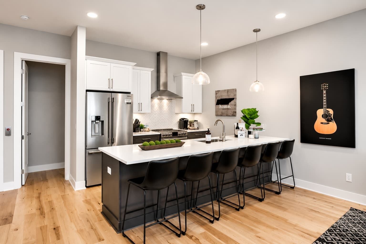 Una cocina moderna con una isla central, electrodomésticos de acero inoxidable, iluminación colgante y una obra de arte con temática de guitarra en la pared.