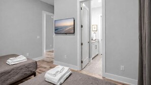 A bedroom with a bed, a bedside table, a folded towel, a painting, and a bathroom visible through an open door.