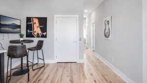 A hallway with a dining area featuring a table and chairs, a white door, and artwork on the walls.