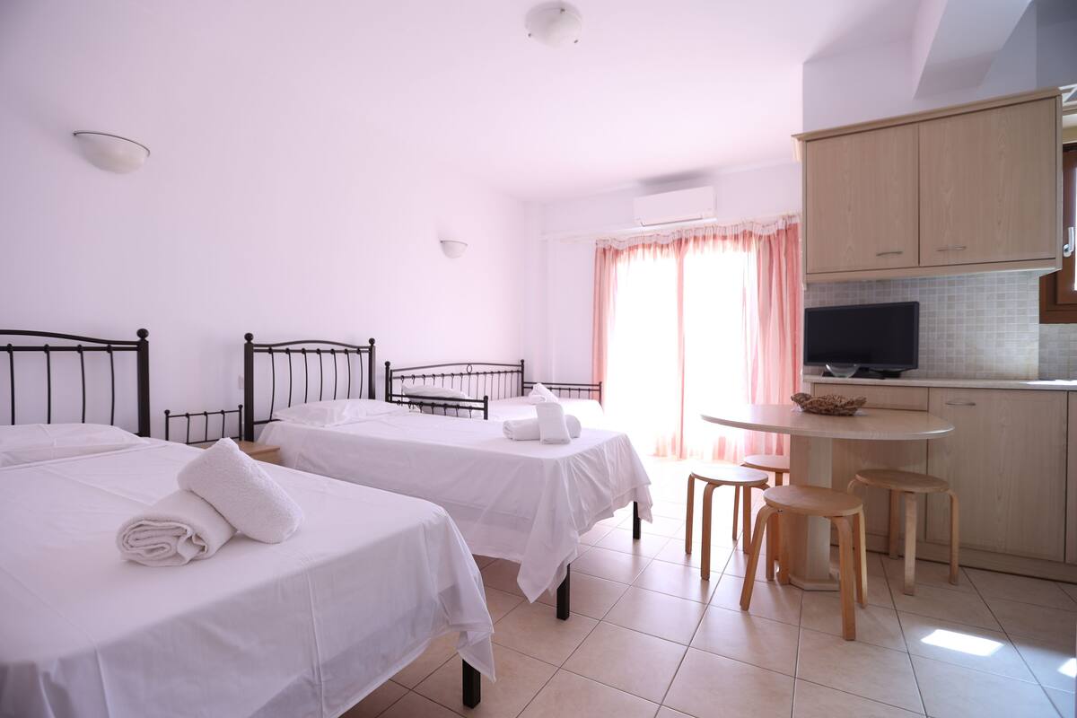 A hotel room with two beds, a small kitchenette, and a dining area.