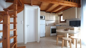 A modern kitchen with wooden beams, white cabinets, a microwave, stove, and a dining area with stools. - Seaside Gialova (Pylos-Nestoras)