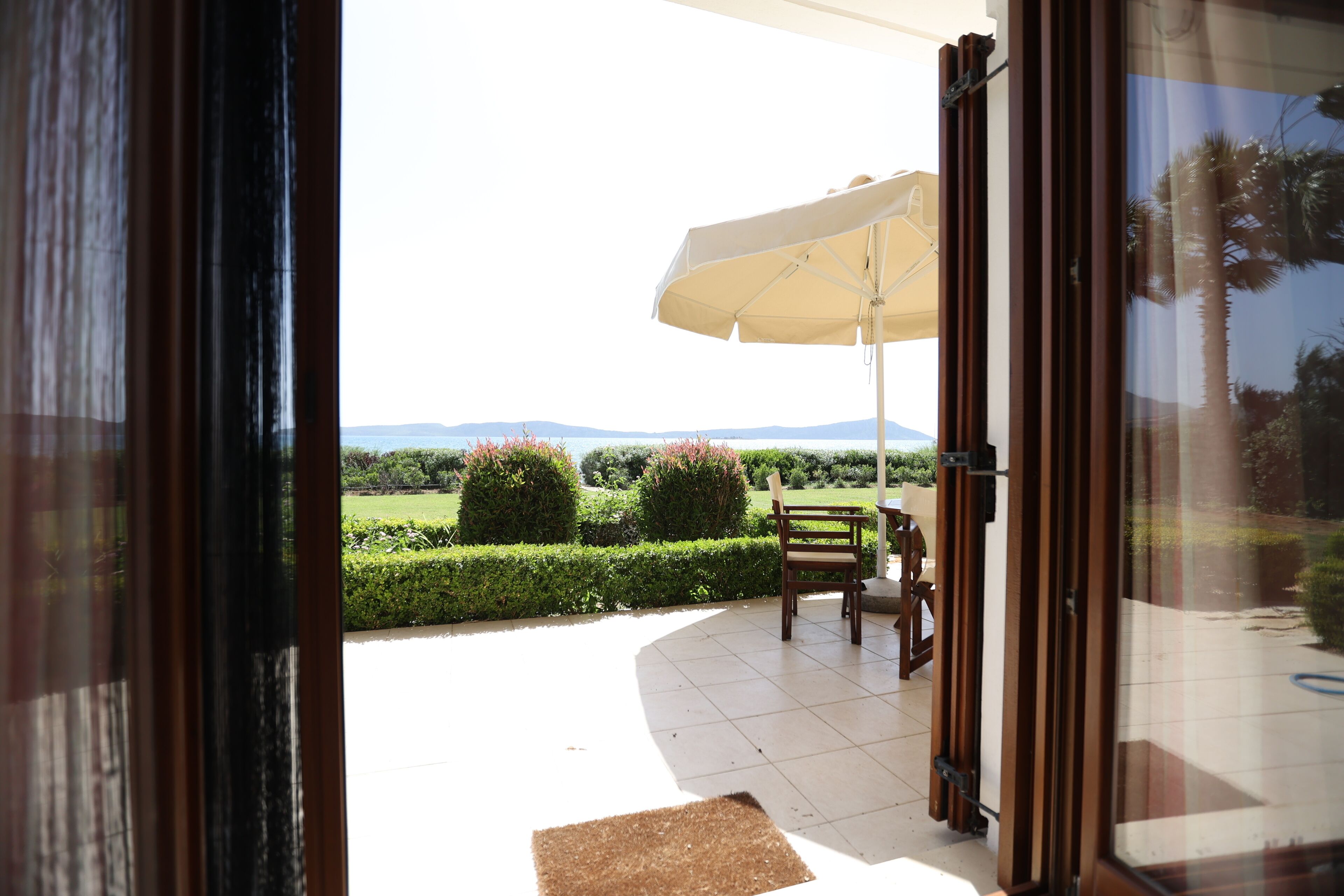 Puerta abierta que da a un patio con mesa, silla y sombrilla.