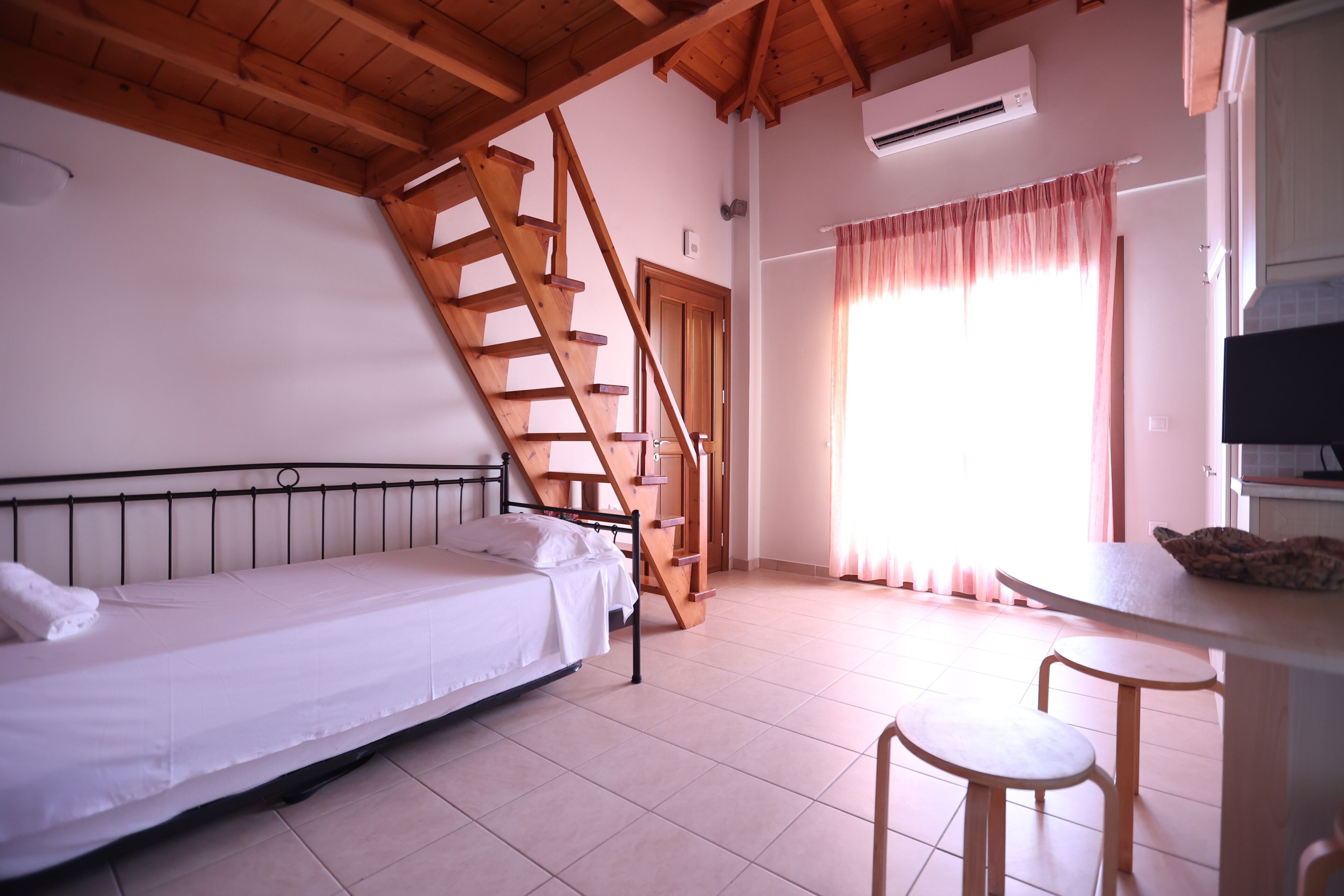Een slaapkamer met een bed, een houten trap, een tafel met twee stoelen en een televisie.