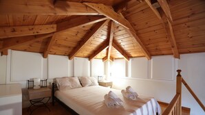 A bedroom with a wooden ceiling, a bed with white linens, two rolled towels on the bed, a nightstand with a lamp, and a wooden staircase. - Seaside Gialova (Pylos-Nestoras)