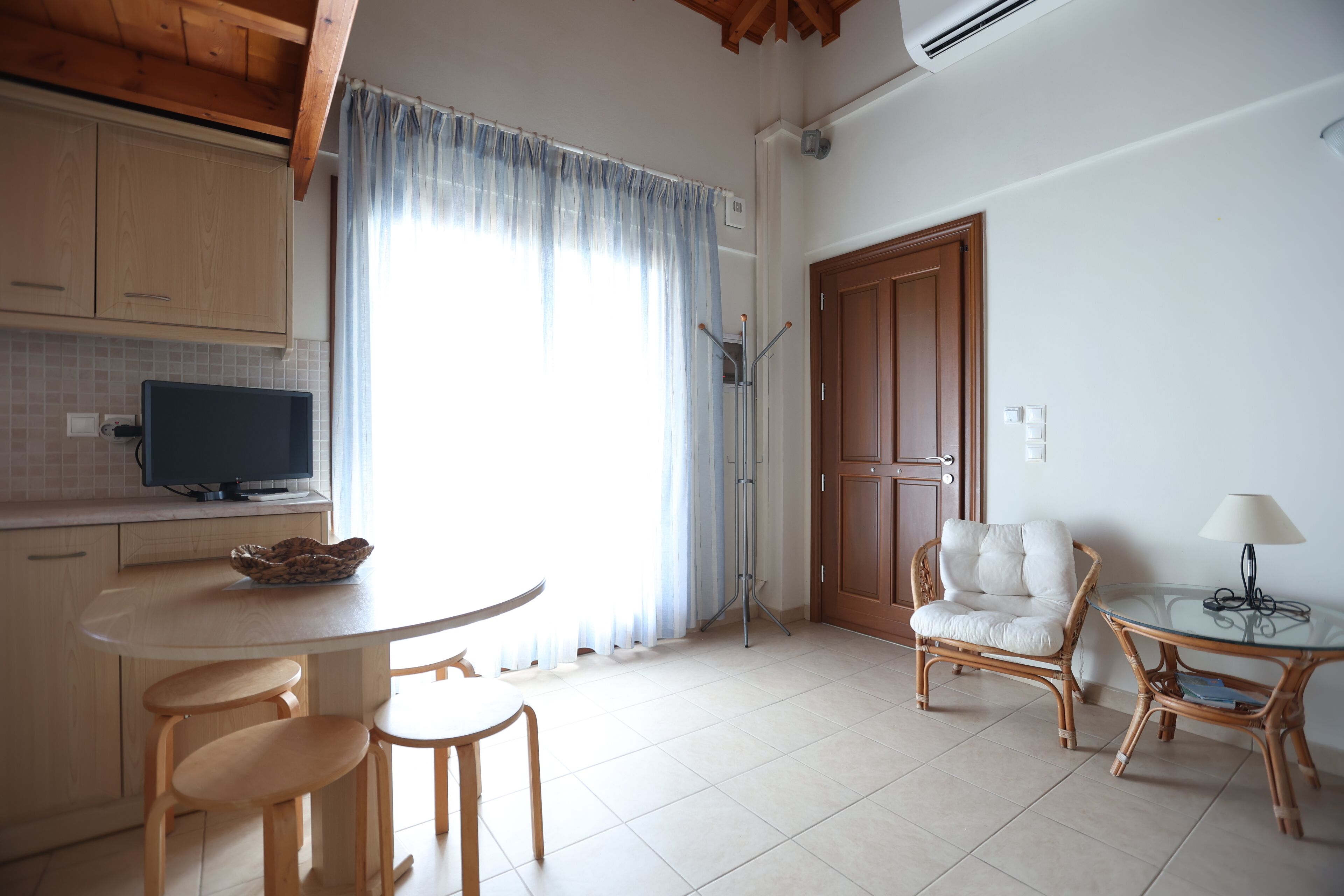 A kitchen with a dining table, chairs, a television, and a wicker chair.