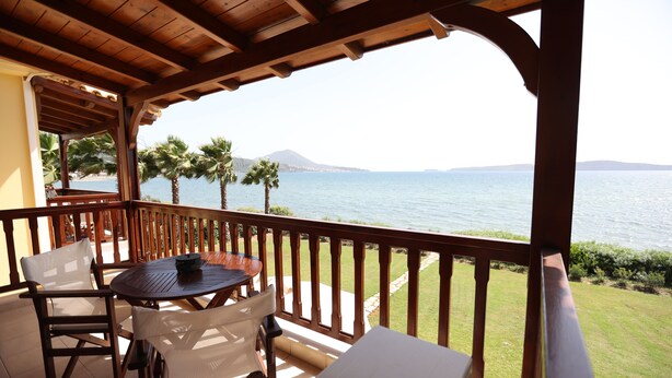 A wooden deck with a table and chairs, overlooking a body of water and palm trees. - Seaside Gialova (Pylos-Nestoras)