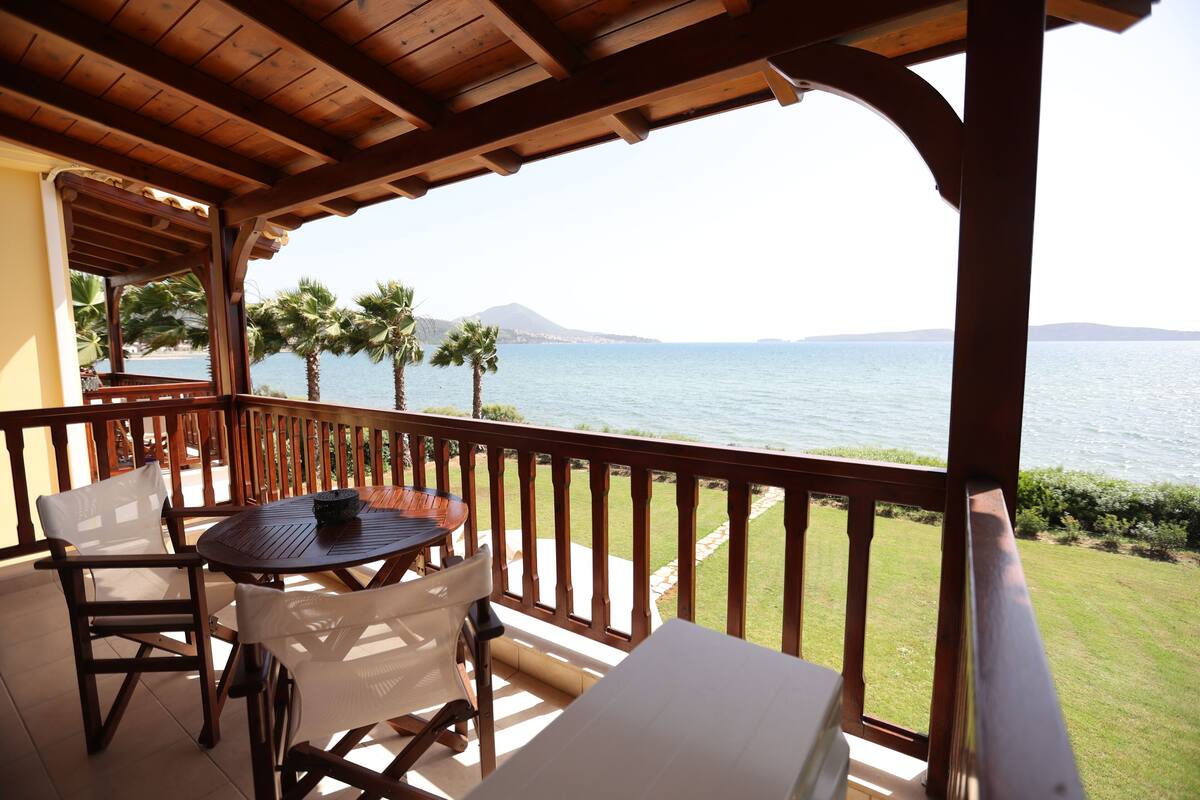 A wooden deck with a table and chairs, overlooking a body of water and palm trees.
