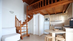 A compact kitchen with wooden staircase, white cabinets, and a small dining area with stools. - Seaside Gialova (Pylos-Nestoras)