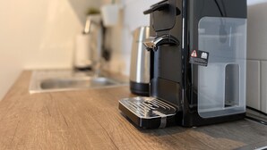 A modern coffee maker on a wooden countertop with a clear water reservoir. - ADN Apartments, modern and minimalist (Koetz)