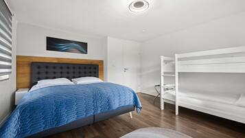 Une chambre avec un lit simple, un lit superposé, un plancher en bois, un luminaire au plafond et une œuvre d’art accrochée au mur.