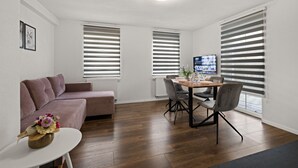A modern living room with a sofa, a dining table with chairs, and a TV on a stand. - ADN Apartments, modern and minimalist (Koetz)