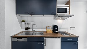 A compact kitchen with dark blue cabinets, a wooden countertop, a built-in microwave, a coffee machine, and a dishwasher. - ADN Apartments, modern and minimalist (Koetz)