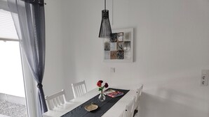 A dining area with a white table, black table runner, and white chairs. There is a vase with a red flower on the table. - Vacation apartment Heide I (Walsrode)