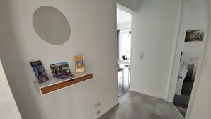 A hallway with a white wall, a round mirror, and a shelf with books. - Vacation apartment Heide I (Walsrode)