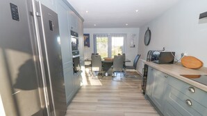 Una cocina moderna con un refrigerador de acero inoxidable, un comedor con mesa y sillas, y vistas al exterior por la ventana.