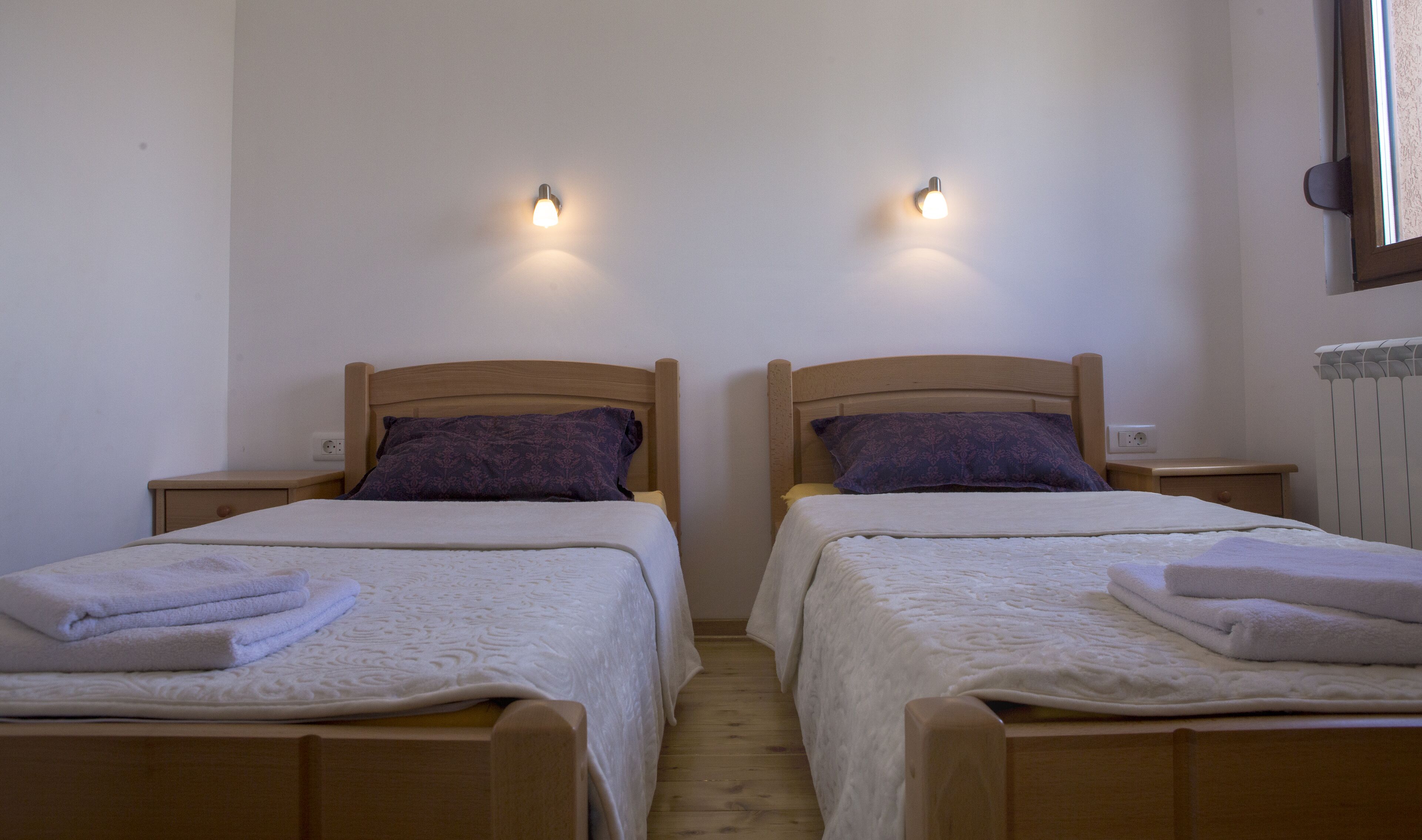 A room with two wooden beds, each with a headboard, a nightstand, and a wall-mounted light.