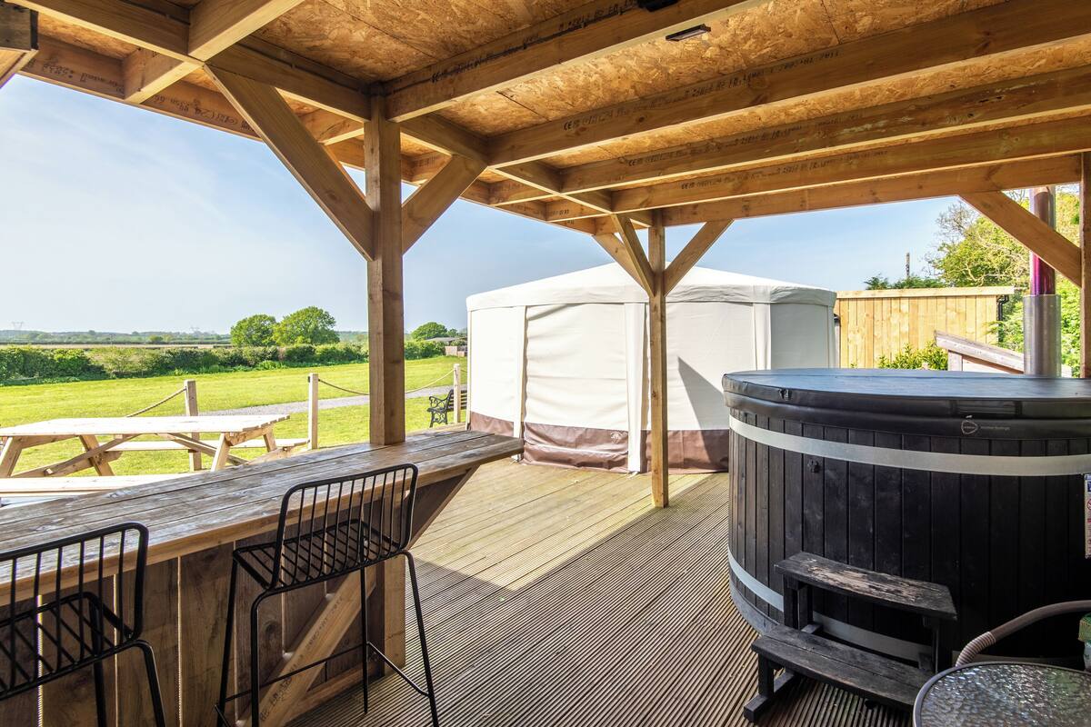 Un patio exterior con vigas de madera, un jacuzzi y un área techada con una mesa y sillas.