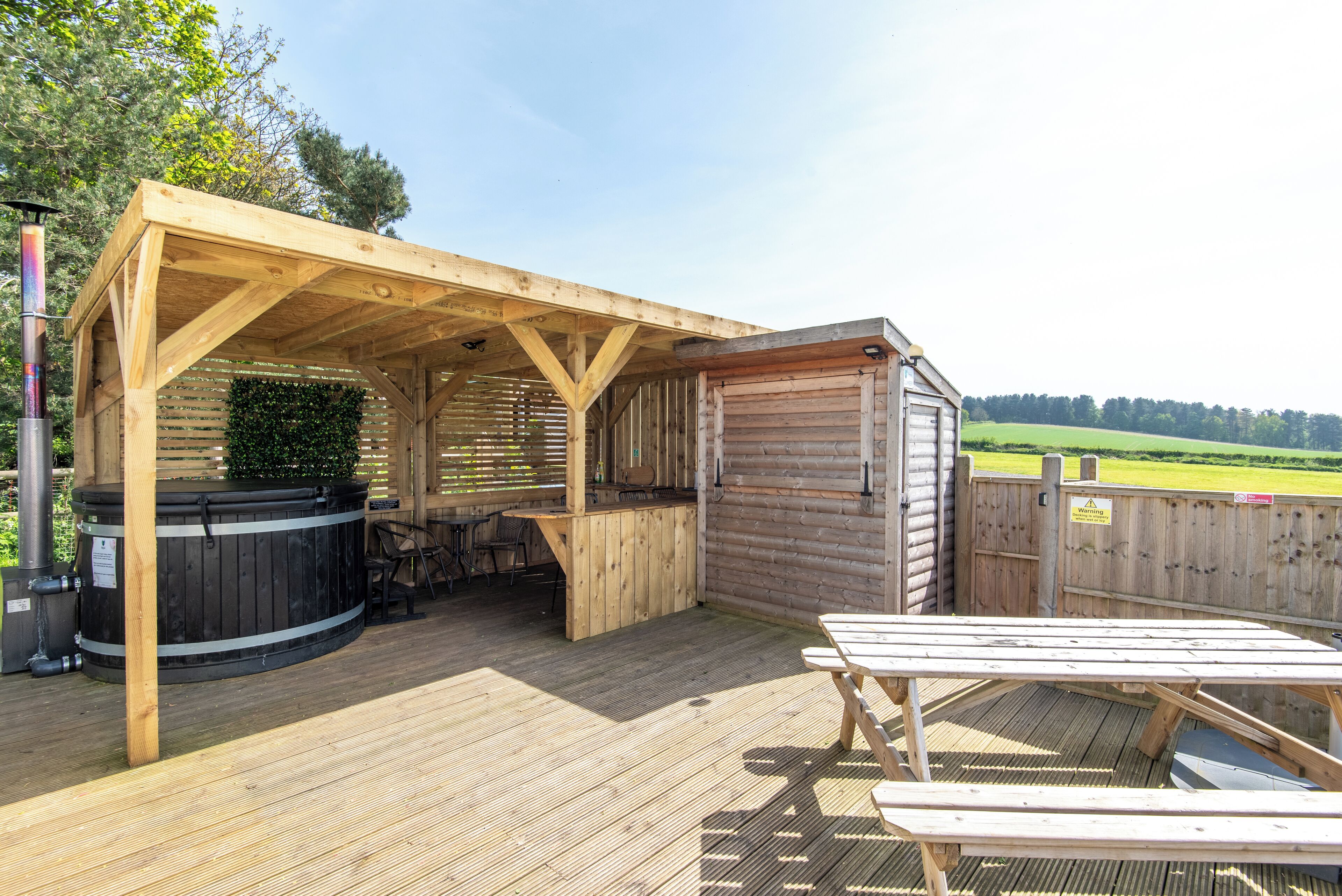 A wooden deck with a hot tub, a barbecue area, and a picnic table.