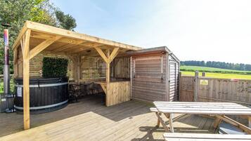 A wooden deck with a hot tub, a barbecue area, and a picnic table.