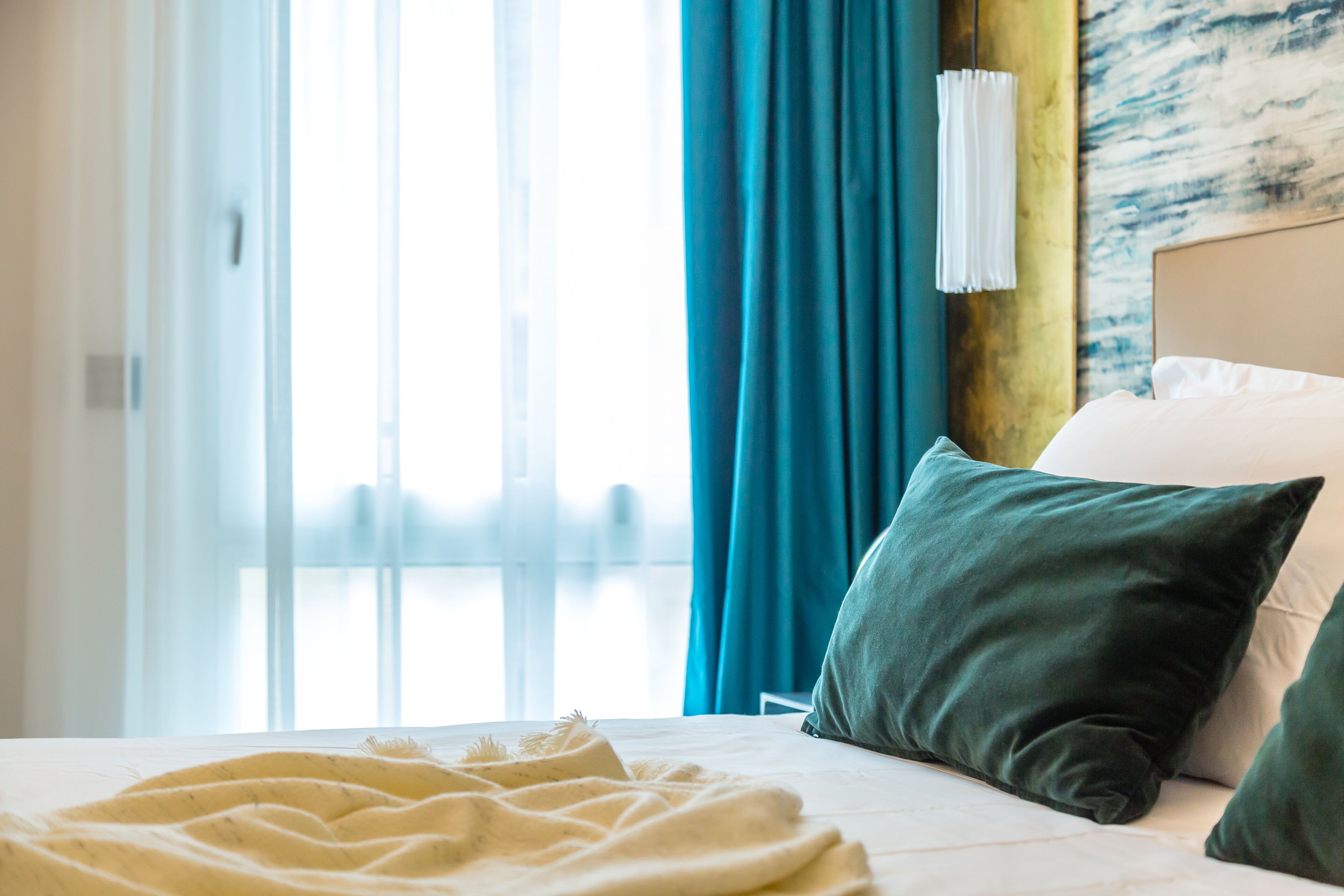 Una habitación de hotel con cama, ventana con cortinas y pared con diseño texturizado.