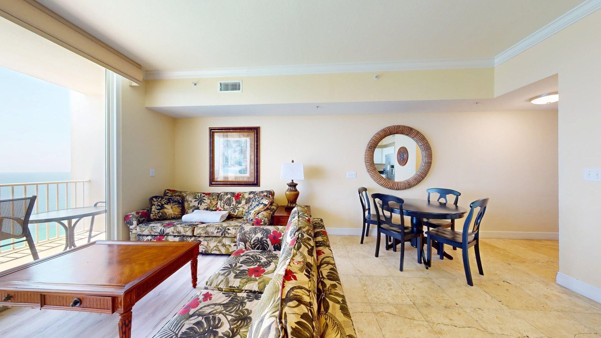 Sala de estar com sofá, mesa de jantar com cadeiras, abajur e quadro na parede.