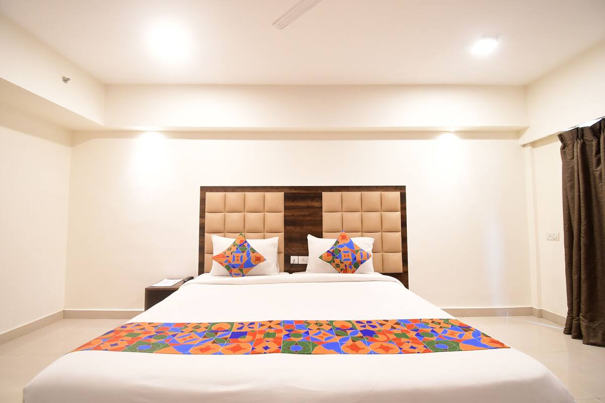 Una habitación de hotel con una cama grande, un cabecero de madera, dos mesitas de noche y una colcha de colores.