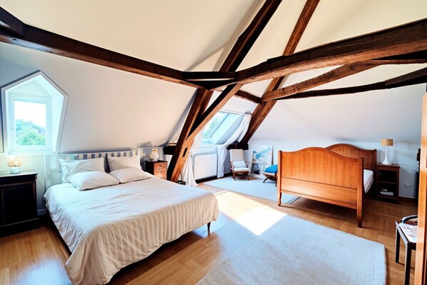 A bedroom with a sloped ceiling, wooden beams, a bed, a chair, and a window.