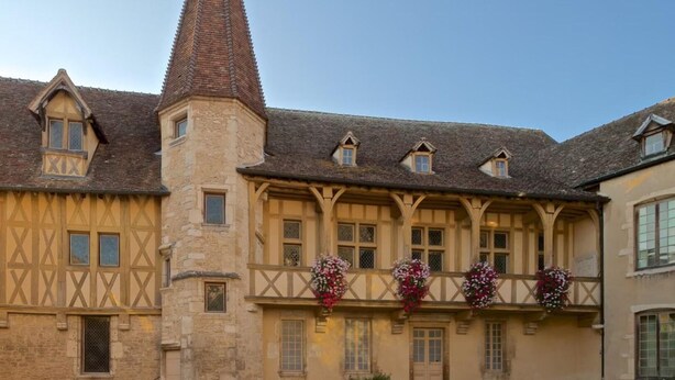 A traditional half-timbered building with a prominent tower, multiple windows, and flower baskets on the balcony. - Charming Burgundy vacation rental with a beautiful pool, sleeps 8—Relaxation guaranteed (Franxault)
