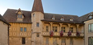 A traditional half-timbered building with a prominent tower, multiple windows, and flower baskets on the balcony.