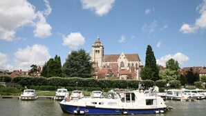 A historic church with a prominent tower, surrounded by a calm river with several boats docked. - Charming Burgundy vacation rental with a beautiful pool, sleeps 8—Relaxation guaranteed (Franxault)